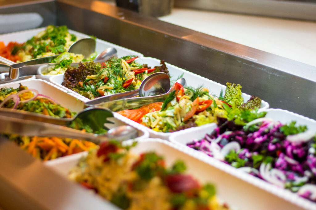 Eine Salatbar mit kleinen viereckigen Salatschüsselchen und Salatbesteck.